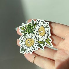 a hand holding a sticker with white and yellow daisies on the back of it