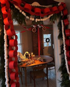 a dining room table decorated for christmas with red and white ribbons on the ceiling, candles in front of it