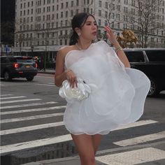 a woman in a white dress is crossing the street with her hand on her hip