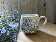 a coffee cup with blue flowers painted on it next to a knitted thrower