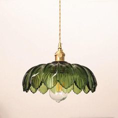 a green glass light hanging from a gold colored ceiling fixture in a room with white walls