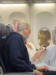 a woman sitting on an airplane looking at her cell phone while another person sits next to her