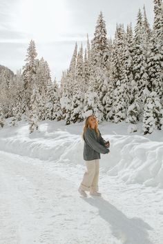 a woman standing in the snow near some trees