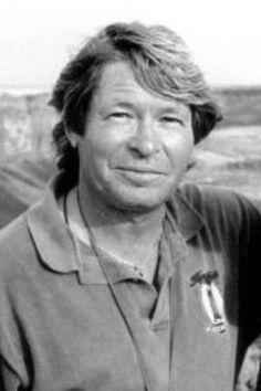 a black and white photo of a man with long hair wearing a polo shirt standing in front of a field