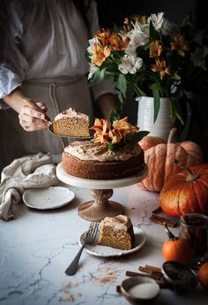 a person is cutting into a cake on a table with flowers and pumpkins in the background