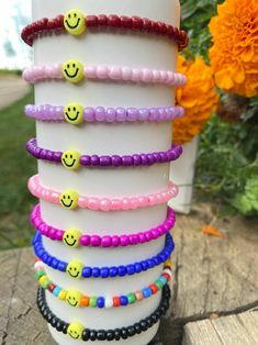 a stack of bracelets with smiley faces on them sitting in front of some flowers