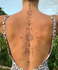 the back of a woman's neck with an intricate tattoo design on her lower back