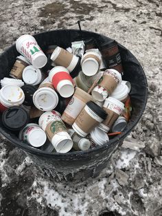 a bucket full of coffee cups sitting on top of snow covered ground