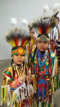 two young children dressed in native american clothing and headdress standing next to each other