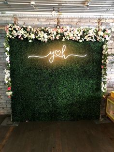 a green wall with white flowers and the word yoh on it is surrounded by greenery