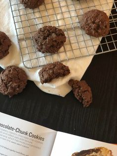 chocolate chunk cookies on a cooling rack with white frosting next to an open cookbook