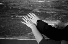 two hands reaching out towards the ocean on a sandy beach with waves crashing in to shore