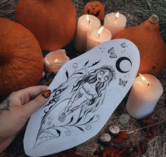 a person holding a paper with a drawing on it next to pumpkins and candles