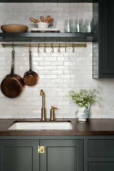 a kitchen with green cabinets and white brick walls, brass handles on the wall, pots and pans hanging above the sink