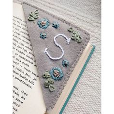 an open book with some flowers on it next to a piece of fabric that has the letter s embroidered onto it