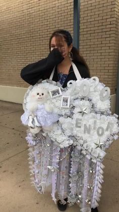 a woman standing next to a building holding a teddy bear in the shape of a heart