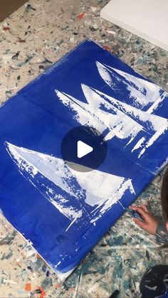 a young boy is painting with white paint on a blue piece of paper that looks like an arrow