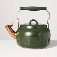 a green tea kettle with a gold handle and an empty cup on the side, sitting on a white surface