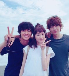 three young people posing for a photo on the beach with their fingers in the air