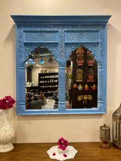 a blue wall mounted mirror on the side of a wall next to a vase with flowers