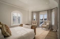 a bedroom with a large bed and two chairs next to a window that looks out onto the water