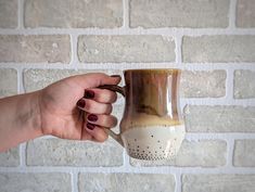 a hand holding a coffee mug in front of a brick wall with white and brown designs