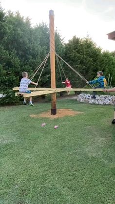 two children are playing on a wooden swing set in the yard with their mom and dad