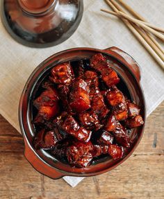 a bowl filled with meat sitting on top of a table next to chopsticks