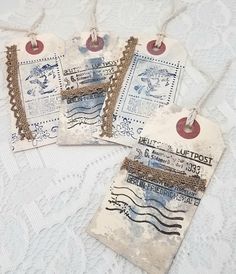 three tags with stamps on them sitting on a lace covered tablecloth and white doily