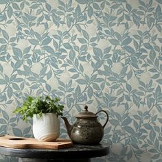 a potted plant sitting on top of a table next to a wall papered with leaves