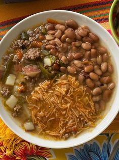 a white bowl filled with beans, meat and vegetables on top of a colorful table cloth