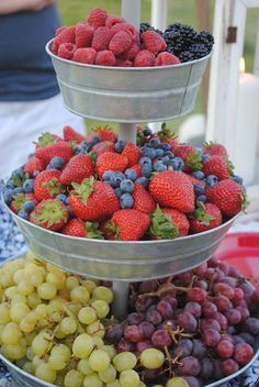 three tiered trays filled with different types of berries and grapes on a table