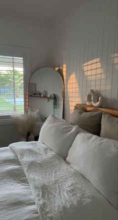 a bed with white linens and pillows in a bedroom next to a large window