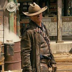 a man wearing a cowboy hat and leather jacket standing in front of an old building