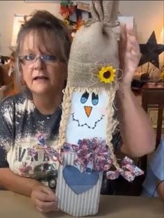 a woman holding up a vase with a face on it and a sunflower sticking out of it