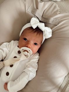 a baby laying on top of a bed wearing a white jacket and bow headband