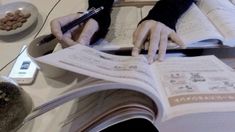 a person sitting at a table with an open book in front of them while holding a pen