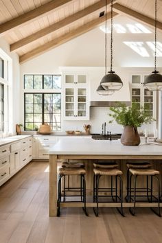 a large kitchen with wooden floors and white cabinets, an island in the middle is surrounded by stools