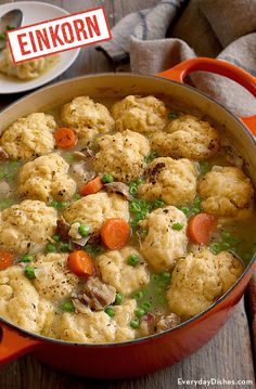 a pot filled with dumplings and carrots on top of a wooden table next to a plate of food