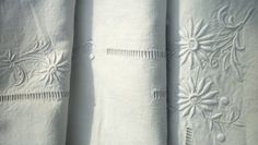 white linens with embroidered designs on them are lined up against a window sill