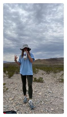 a woman standing on top of a gravel covered field holding a cup in her hand