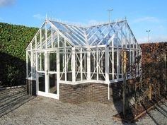 a glass house sitting on top of a gravel road next to a hedge covered field