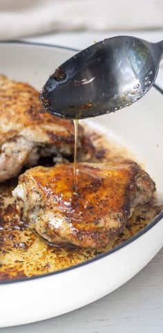 a person pouring sauce on some meat in a bowl with a spoon and fork next to it