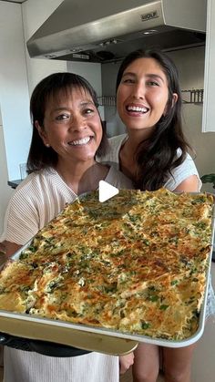 two women are holding up a large casserole