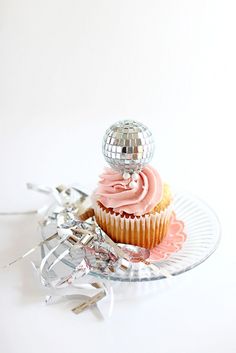 a cupcake with pink frosting and a disco ball on top sitting on a plate