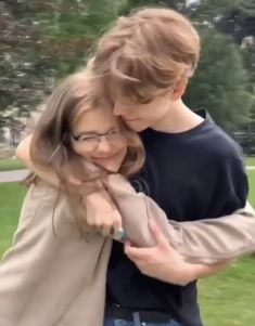 a boy and girl hugging each other in the park