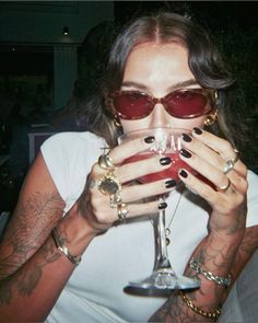 a woman wearing sunglasses and holding a wine glass in front of her face with both hands