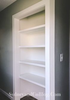 an empty book shelf in the corner of a room with gray walls and white shelves