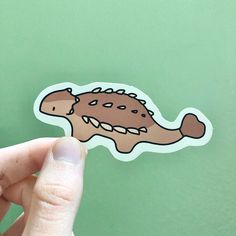 a hand holding up a sticker with an image of a dinosaur on it's face