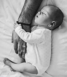 a black and white photo of a baby holding the arm of an adult